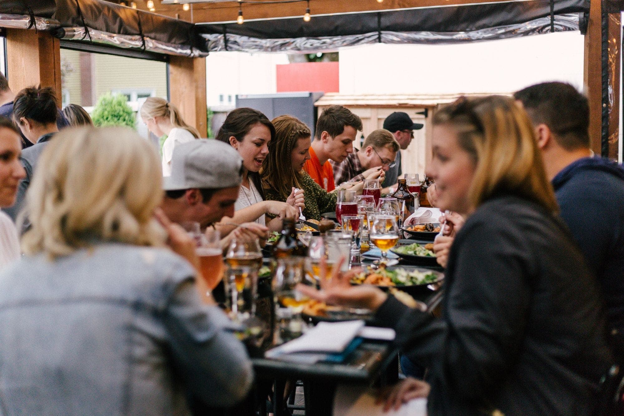 Friends sharing dinner and drinks at a long table on a covered patio