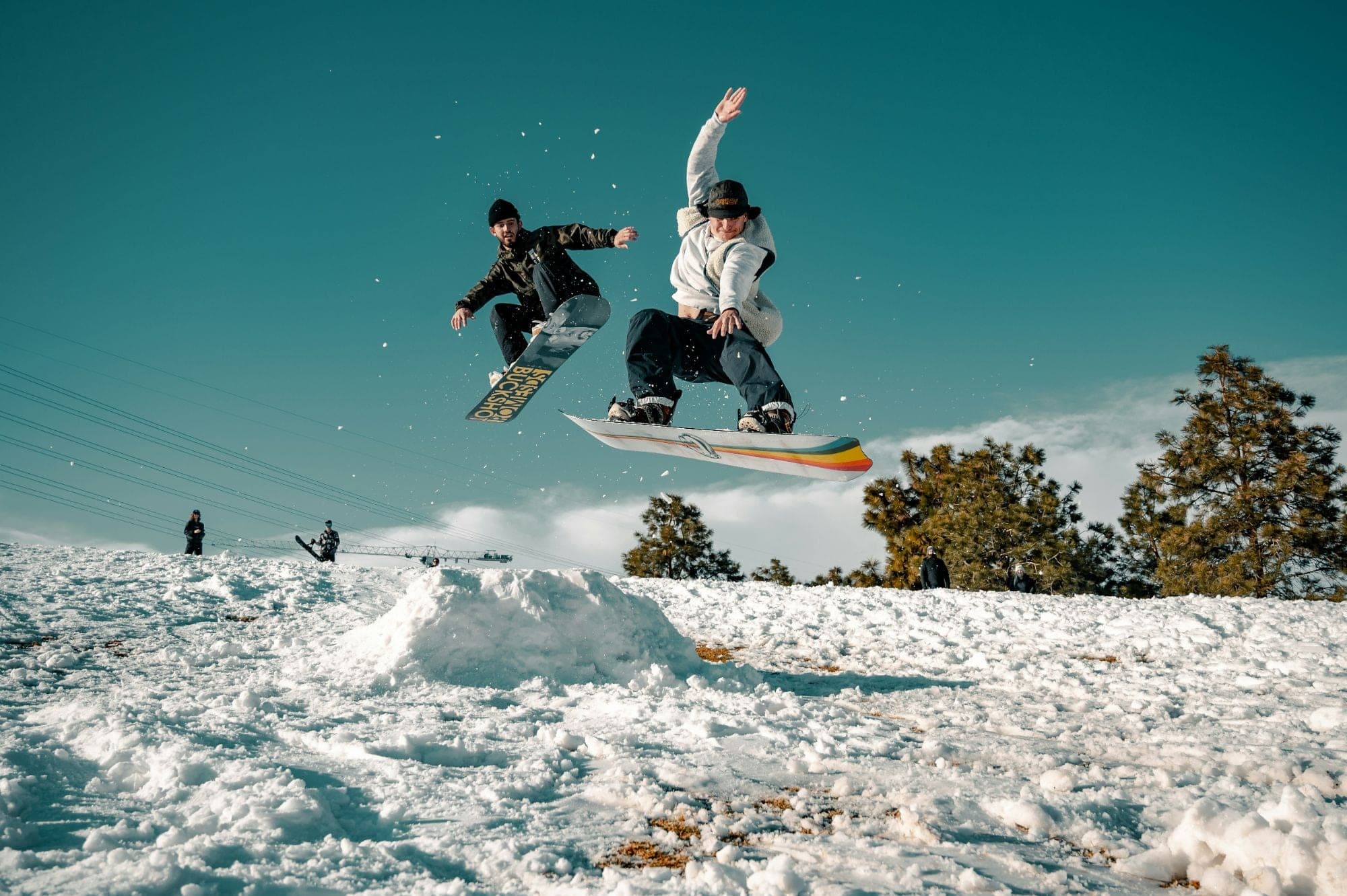 Two friends mid-air on snowboards over a jump on a sunny hill